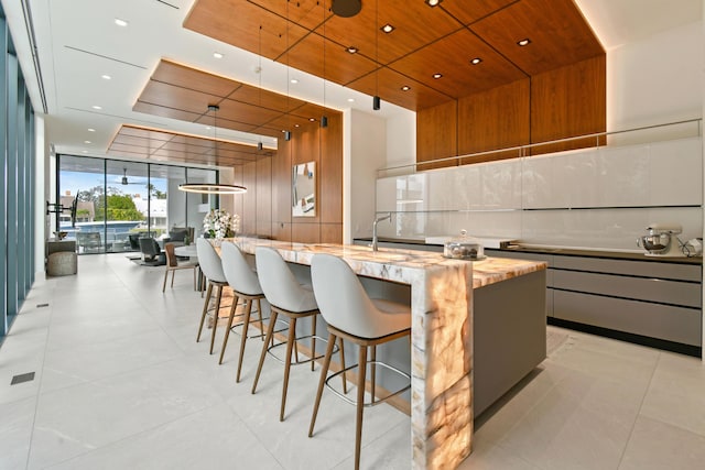 kitchen with expansive windows, wooden ceiling, modern cabinets, and a large island with sink