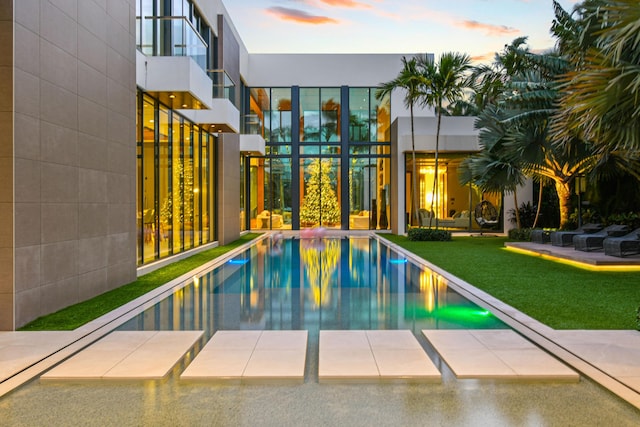 pool at dusk featuring a lawn