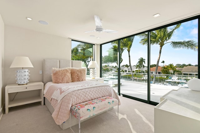 bedroom with ceiling fan, light colored carpet, a water view, access to exterior, and expansive windows