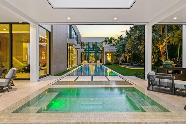 pool at dusk with a hot tub and a patio area