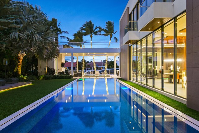 pool at dusk with an outdoor pool and a yard