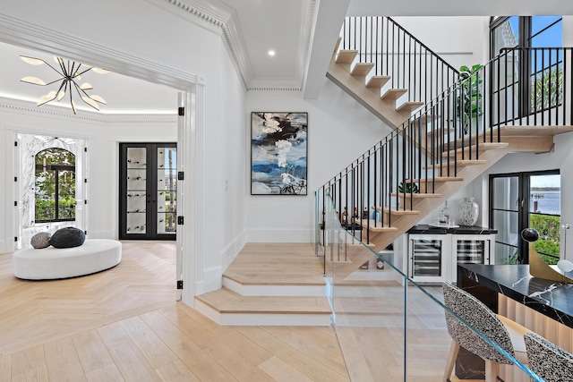 entrance foyer featuring french doors, beverage cooler, ornamental molding, and a notable chandelier