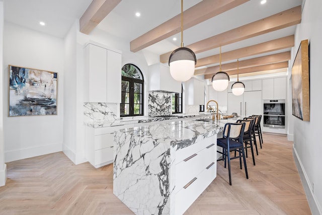 kitchen with pendant lighting, white cabinets, a spacious island, light stone countertops, and beamed ceiling