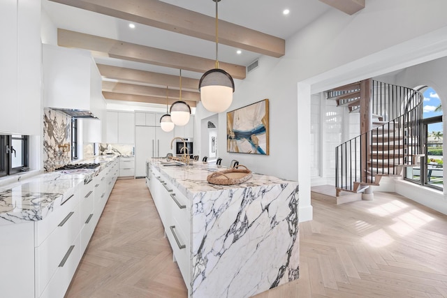 kitchen with a large island with sink, white cabinets, hanging light fixtures, beam ceiling, and light parquet flooring