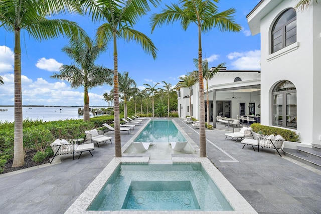 view of pool with an in ground hot tub, a patio, a water view, and ceiling fan