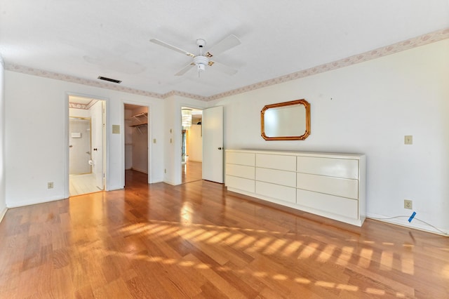 unfurnished bedroom featuring a closet, a walk in closet, light hardwood / wood-style floors, and ceiling fan