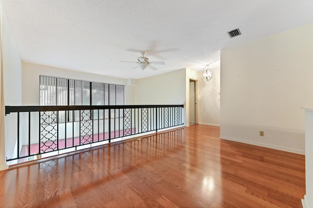 spare room with a textured ceiling, hardwood / wood-style floors, and ceiling fan with notable chandelier