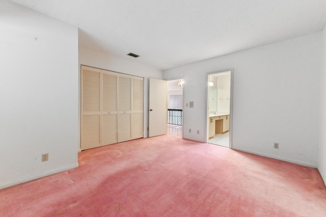 unfurnished bedroom with ensuite bathroom, a closet, and light colored carpet