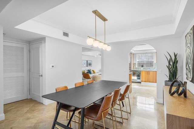 dining space with a raised ceiling, ornamental molding, and beverage cooler