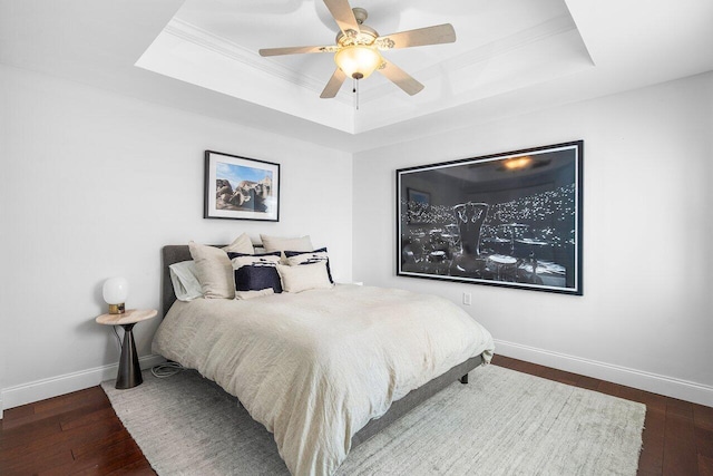 bedroom with a tray ceiling, ceiling fan, crown molding, and dark wood-type flooring