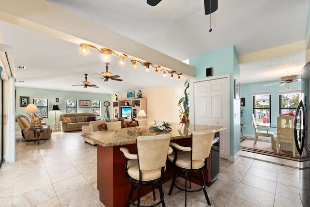 kitchen featuring a kitchen island, light stone counters, stainless steel fridge, a breakfast bar, and light tile patterned flooring