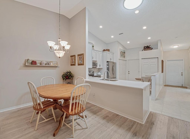 dining room with light wood-type flooring, high vaulted ceiling, an inviting chandelier, and sink