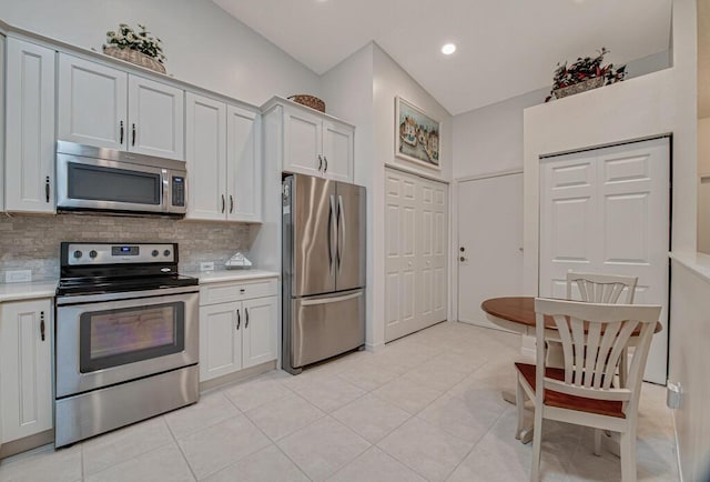 kitchen featuring backsplash, stainless steel appliances, light tile patterned floors, white cabinetry, and lofted ceiling