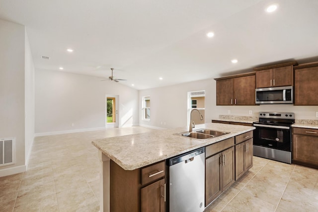 kitchen with light stone countertops, ceiling fan, sink, stainless steel appliances, and a center island with sink