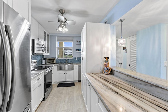 kitchen featuring white cabinets, sink, appliances with stainless steel finishes, decorative light fixtures, and light hardwood / wood-style floors