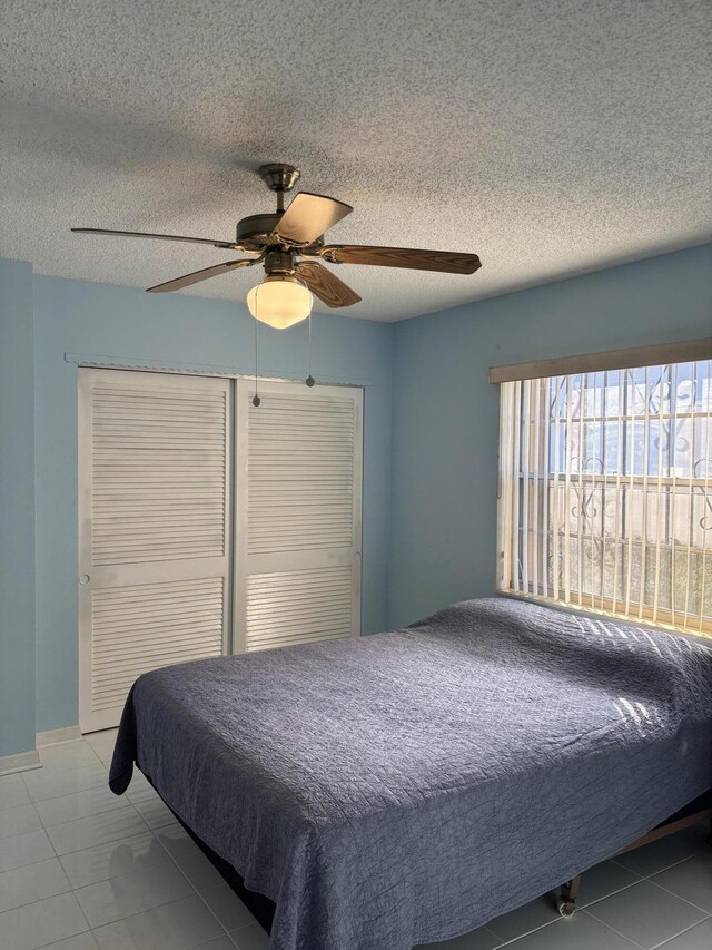 tiled bedroom with ceiling fan and a textured ceiling