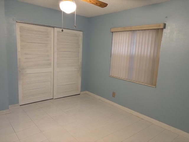 unfurnished bedroom featuring ceiling fan, a closet, light tile patterned floors, and a textured ceiling