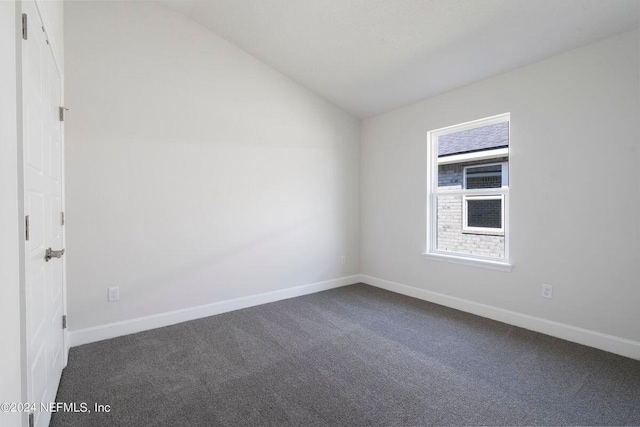 empty room featuring vaulted ceiling and dark colored carpet