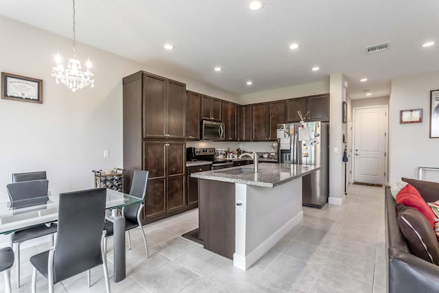 kitchen with hanging light fixtures, light stone countertops, an island with sink, appliances with stainless steel finishes, and a notable chandelier