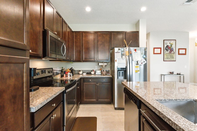 kitchen featuring light stone counters, dark brown cabinetry, stainless steel appliances, a textured ceiling, and light tile patterned floors