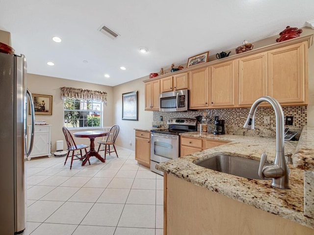 kitchen with appliances with stainless steel finishes, light stone counters, light brown cabinetry, and sink