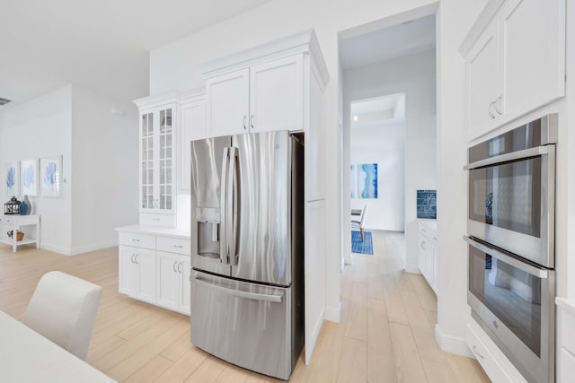 kitchen with stainless steel appliances, white cabinetry, and light hardwood / wood-style floors