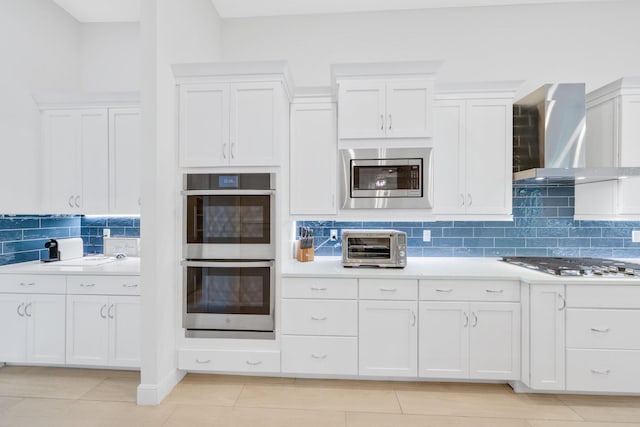 kitchen with white cabinets, wall chimney range hood, stainless steel appliances, and tasteful backsplash