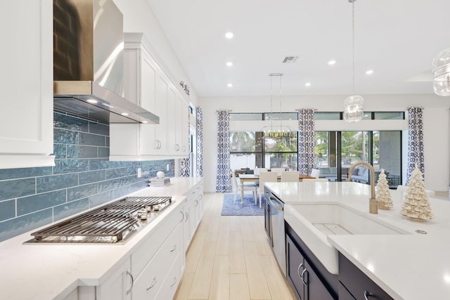 kitchen featuring white cabinets, pendant lighting, stainless steel appliances, and wall chimney exhaust hood