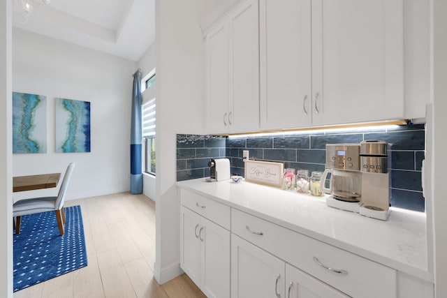 kitchen with white cabinets, decorative backsplash, light hardwood / wood-style floors, and light stone countertops