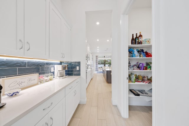 kitchen with white cabinets, decorative backsplash, and light wood-type flooring