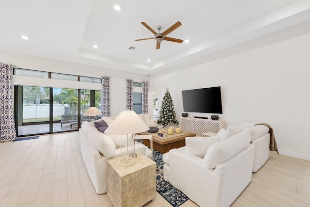 living room featuring a tray ceiling, ceiling fan, and light hardwood / wood-style floors