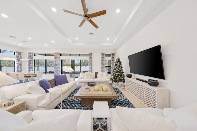 living room with a raised ceiling, ceiling fan, and plenty of natural light