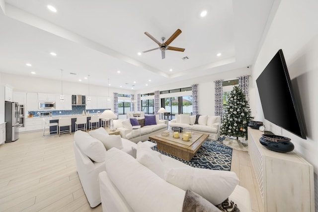 living room with ceiling fan, light hardwood / wood-style floors, and a raised ceiling