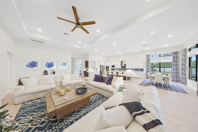 living room with light hardwood / wood-style floors, ceiling fan, and a tray ceiling