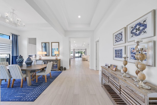 hallway featuring an inviting chandelier, light hardwood / wood-style flooring, plenty of natural light, and a tray ceiling