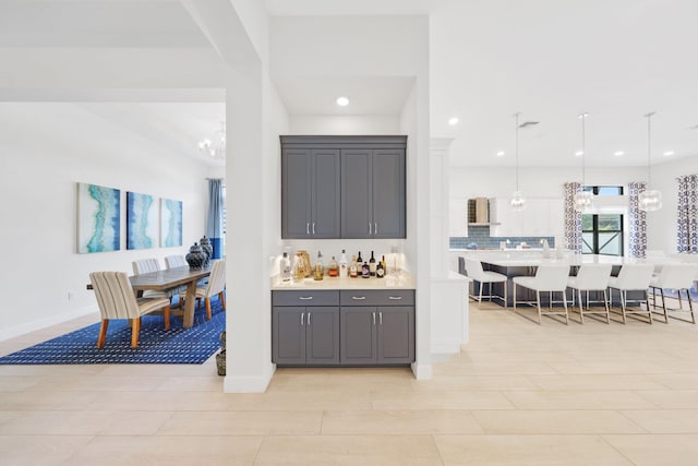 kitchen featuring a kitchen bar, pendant lighting, backsplash, and gray cabinets