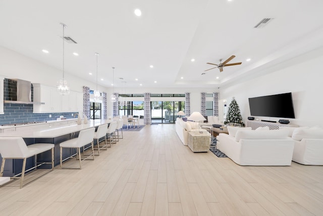 living room featuring a raised ceiling, ceiling fan, and light hardwood / wood-style flooring