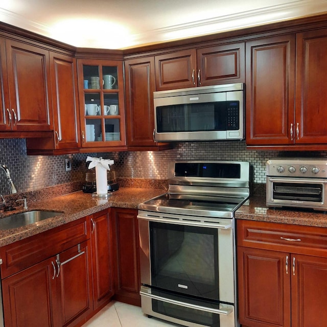 kitchen featuring sink, stainless steel appliances, backsplash, dark stone counters, and light tile patterned flooring