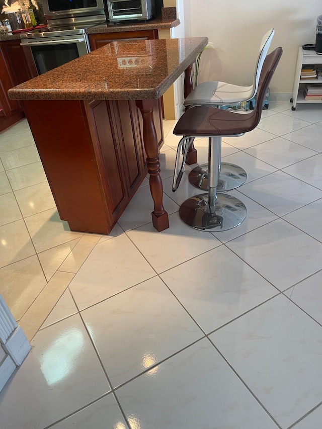 kitchen with stainless steel oven, a kitchen bar, light tile patterned floors, and a kitchen island