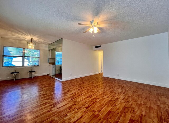 unfurnished living room featuring ceiling fan with notable chandelier, a textured ceiling, and hardwood / wood-style flooring