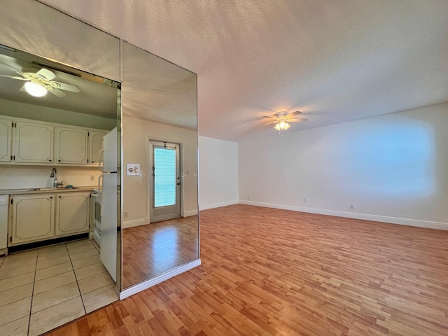 unfurnished living room featuring ceiling fan, sink, a textured ceiling, and light hardwood / wood-style flooring