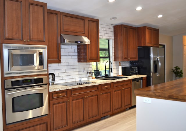 kitchen featuring backsplash, exhaust hood, black appliances, sink, and light stone counters