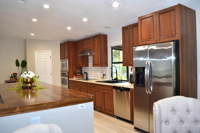 kitchen featuring sink, tasteful backsplash, light hardwood / wood-style flooring, range hood, and appliances with stainless steel finishes