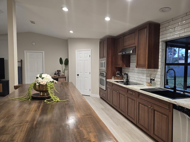 kitchen with sink, stainless steel appliances, light stone counters, backsplash, and vaulted ceiling