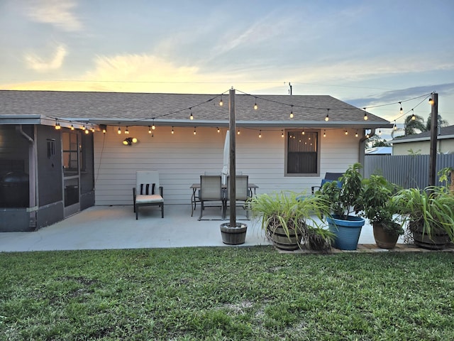 back house at dusk with a sunroom, a patio area, and a yard