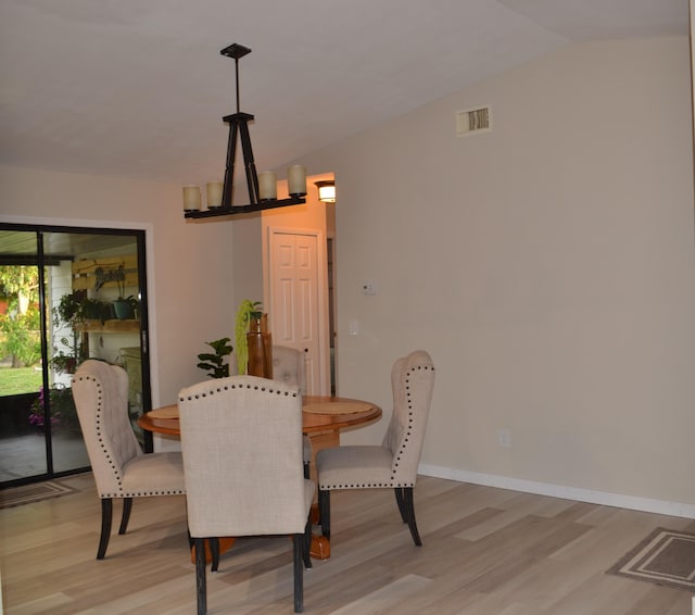 dining space with a chandelier, vaulted ceiling, and light hardwood / wood-style flooring