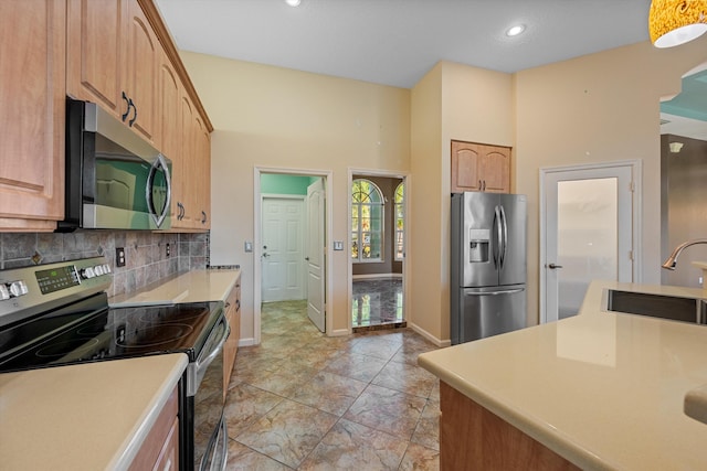 kitchen with sink, light brown cabinets, stainless steel appliances, a towering ceiling, and decorative backsplash