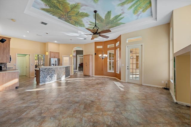 unfurnished living room with ceiling fan with notable chandelier, a tray ceiling, and a wealth of natural light