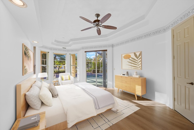 bedroom featuring hardwood / wood-style floors, access to outside, ceiling fan, and a tray ceiling