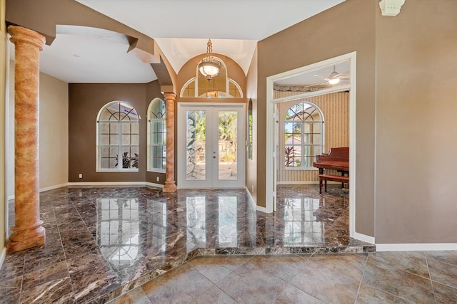 foyer with french doors, ceiling fan with notable chandelier, and decorative columns